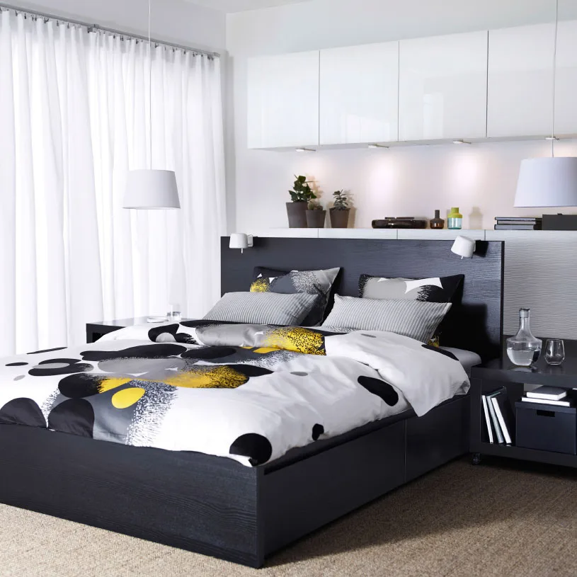 A bedroom with a black brown MALM bed, BESTÅ storage with yellow doors and BOLLTISTEL quilt cover