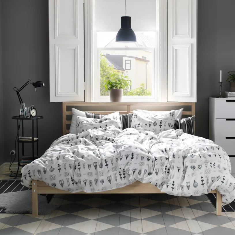 A rustic bedroom with a FJELLSE bed in untreated wood, SÖTVÄPPLING graphic quilt cover in white and black and GUNNERN pedestal table